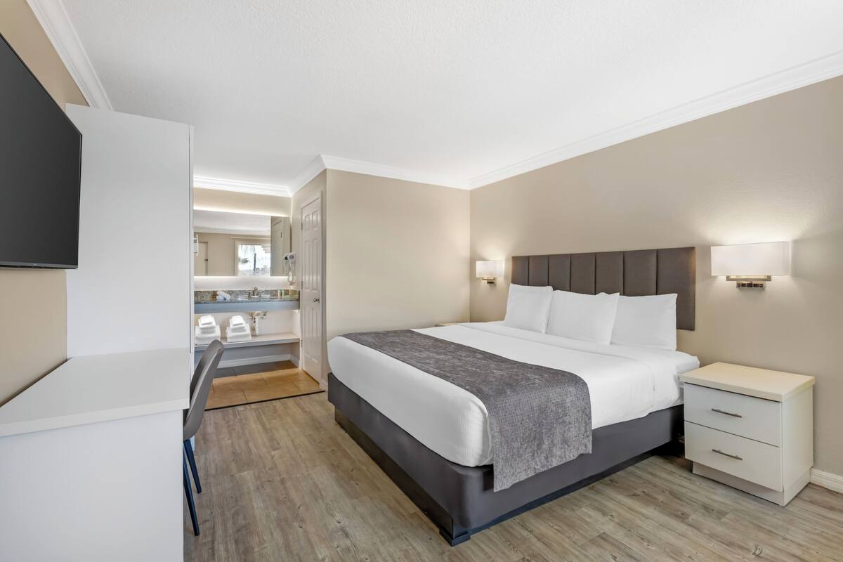 Ein modernes Hotelzimmer mit einem großen Bett, Nachttischen, einem Schreibtisch und einem Spiegel.