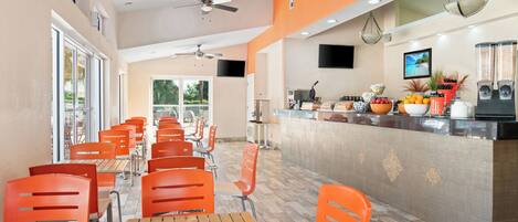 A restaurant with orange chairs and wooden tables, a counter with food and drinks, and a TV mounted on the wall.