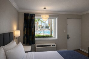 Ein Hotelzimmer mit Bett, einem Vorhangfenster, Blick auf einen Pool, einer Tür und einer Wand-Klimaanlage.