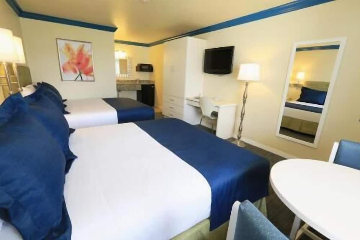 Ein Hotelzimmer mit zwei Betten, einem Schreibtisch, einem Sessel, einem Fernseher und einem Fenster.