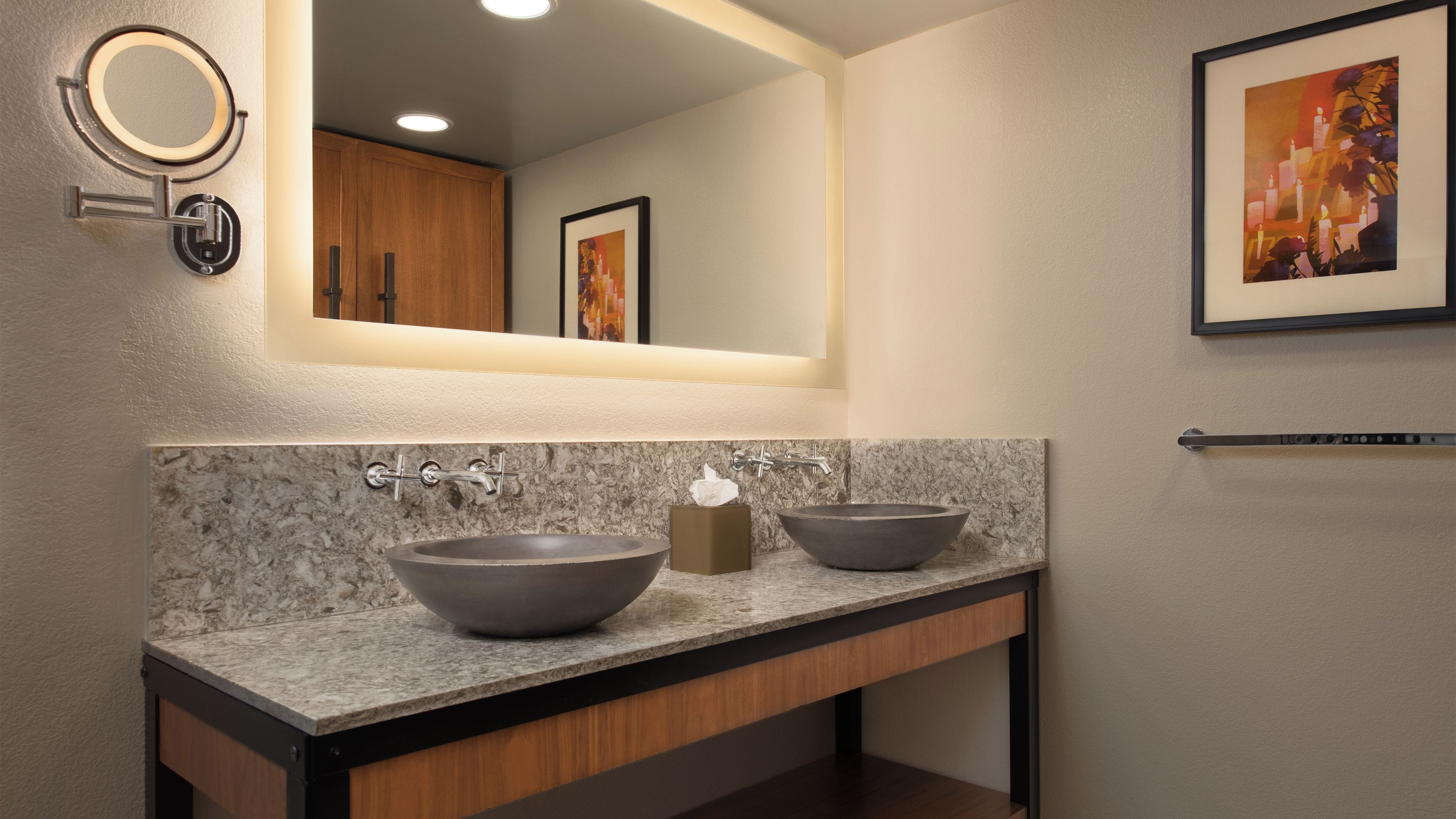 A bathroom with two vessel sinks, a mirror, and a framed artwork on the wall.