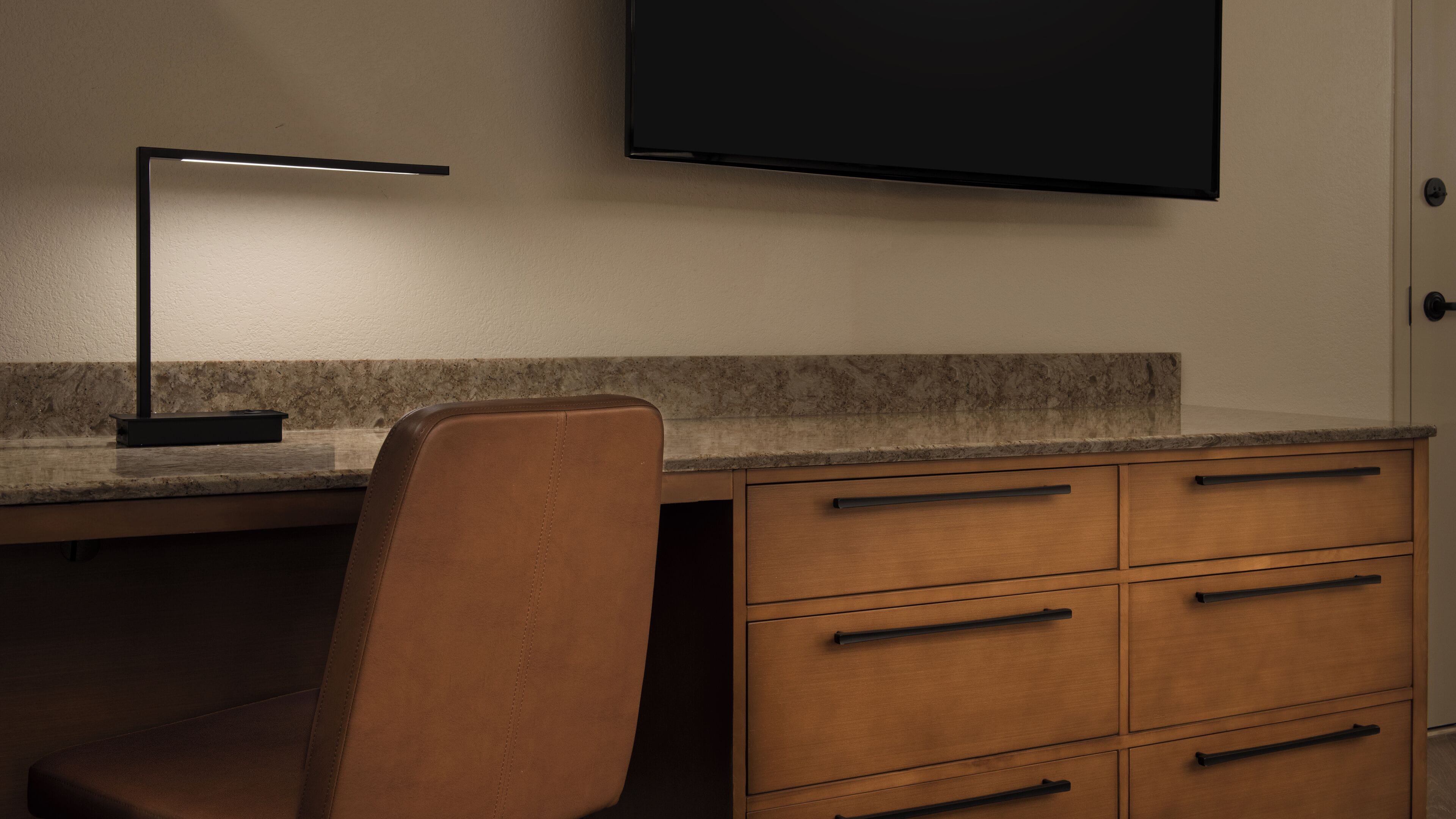 A workspace with a desk, chair, and a flat-screen TV mounted on the wall.