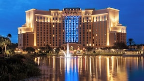 A large, illuminated hotel with a central fountain, reflecting in a calm body of water. - Disney's Coronado Springs Resort (Lake Buena Vista)