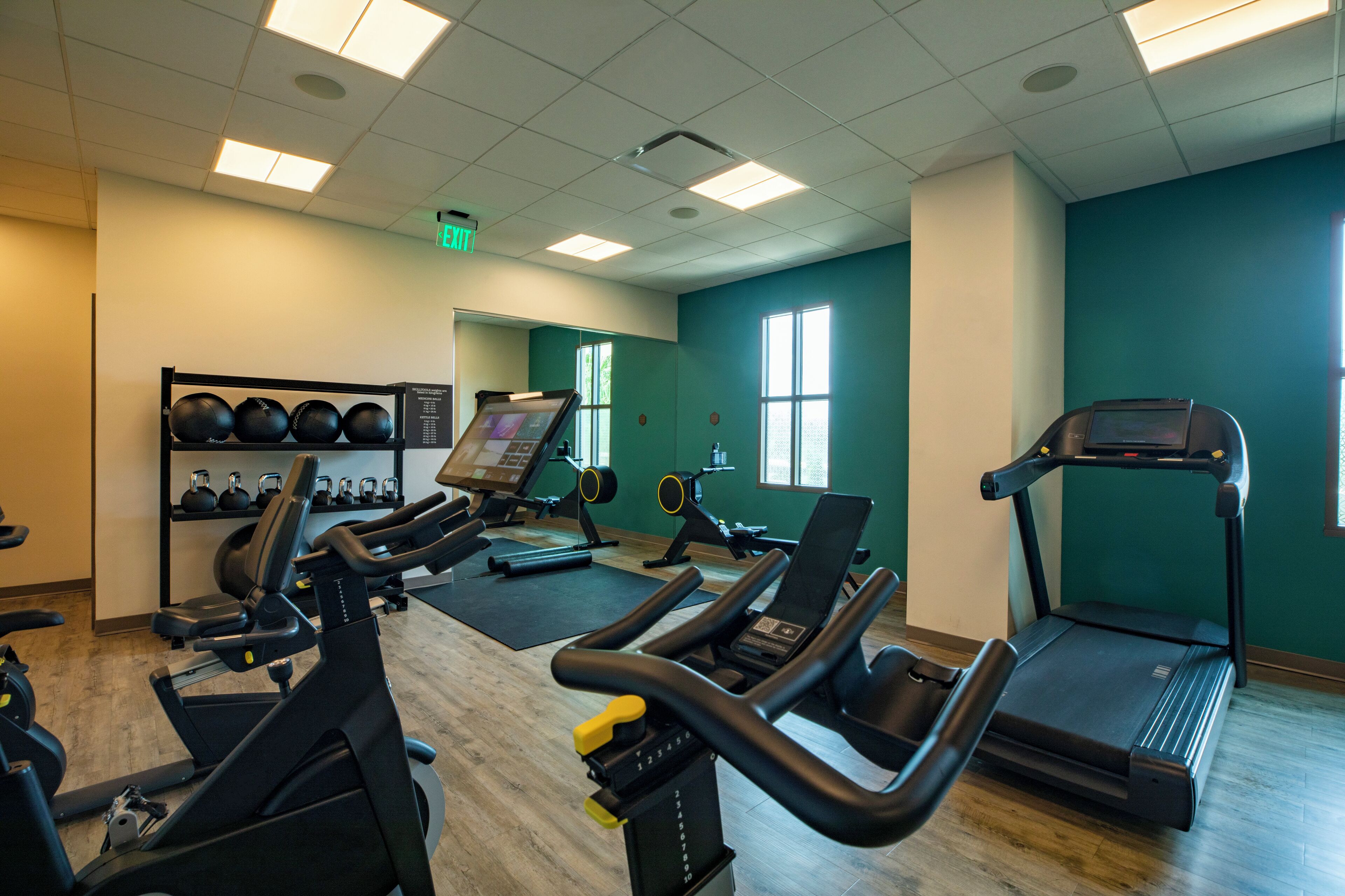 A gym with exercise equipment, a wall-mounted screen, and a window.