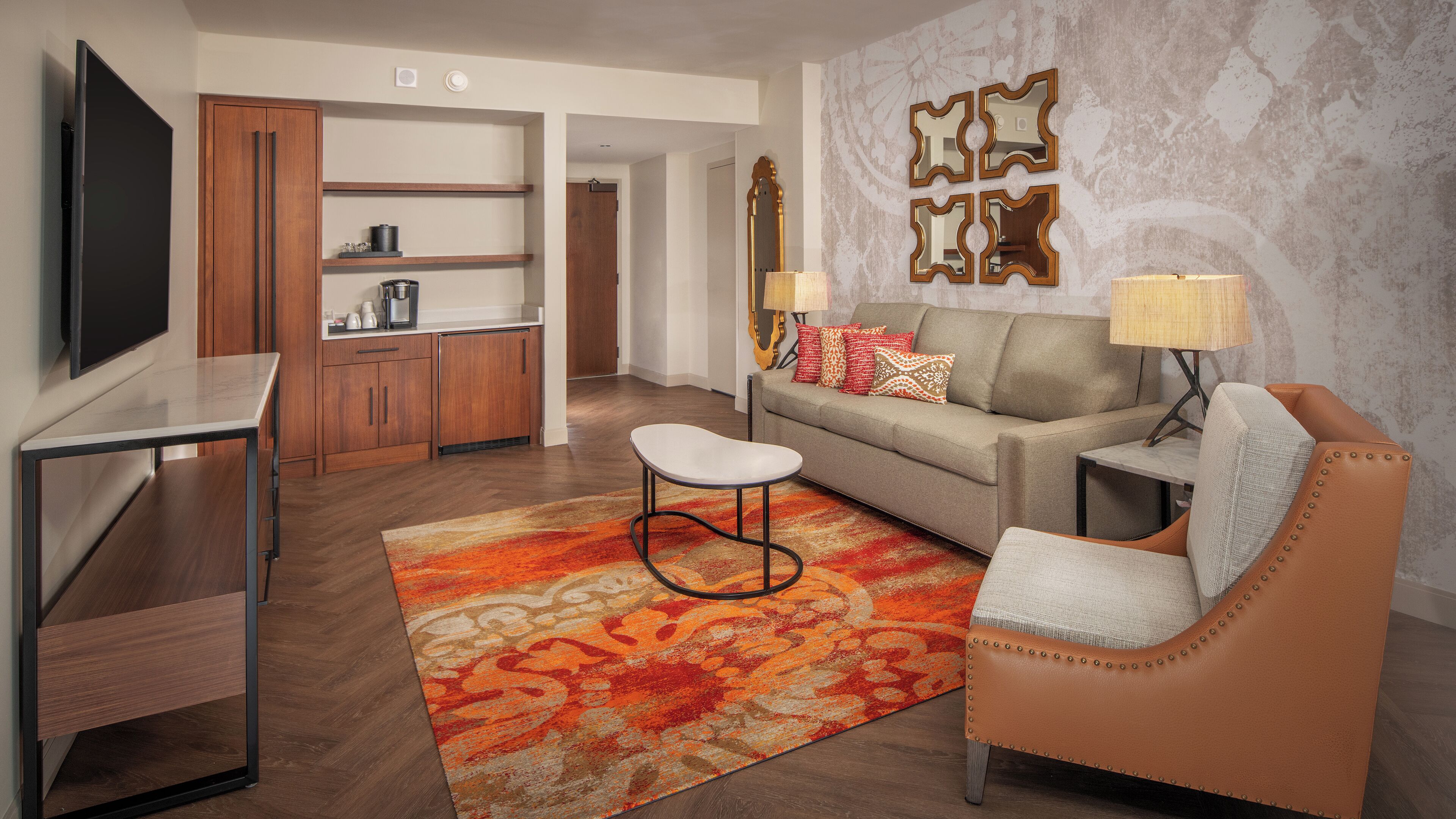 Una sala de estar moderna con sofá, sillón, mesa de centro y televisor. Cuenta con una zona de cocina con armarios y encimera.