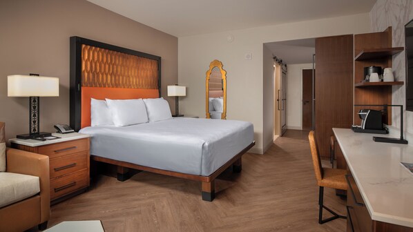A hotel room with a bed, bedside table, lamp, chair, desk, and a wardrobe.