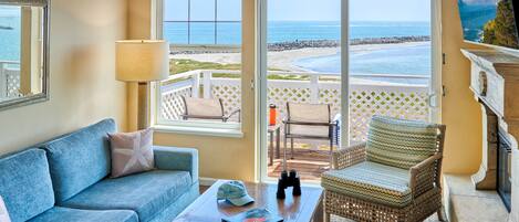 Una habitación con sofá azul, una silla de mimbre, una mesita de centro y vistas a la playa y al océano.