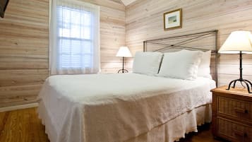 A bedroom with a wooden wall, a bed with white bedding, two bedside lamps, and a small bedside table.
