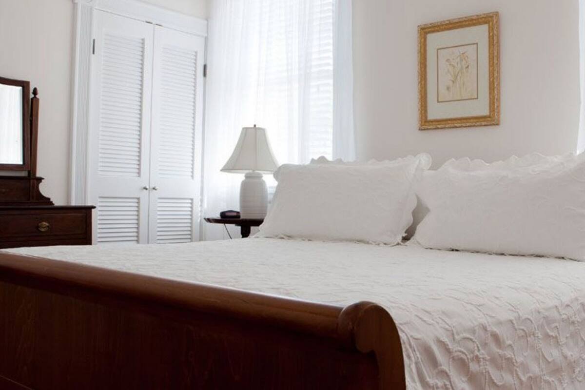 A neatly made bed with white linens, a wooden headboard, and a nightstand with a lamp.
