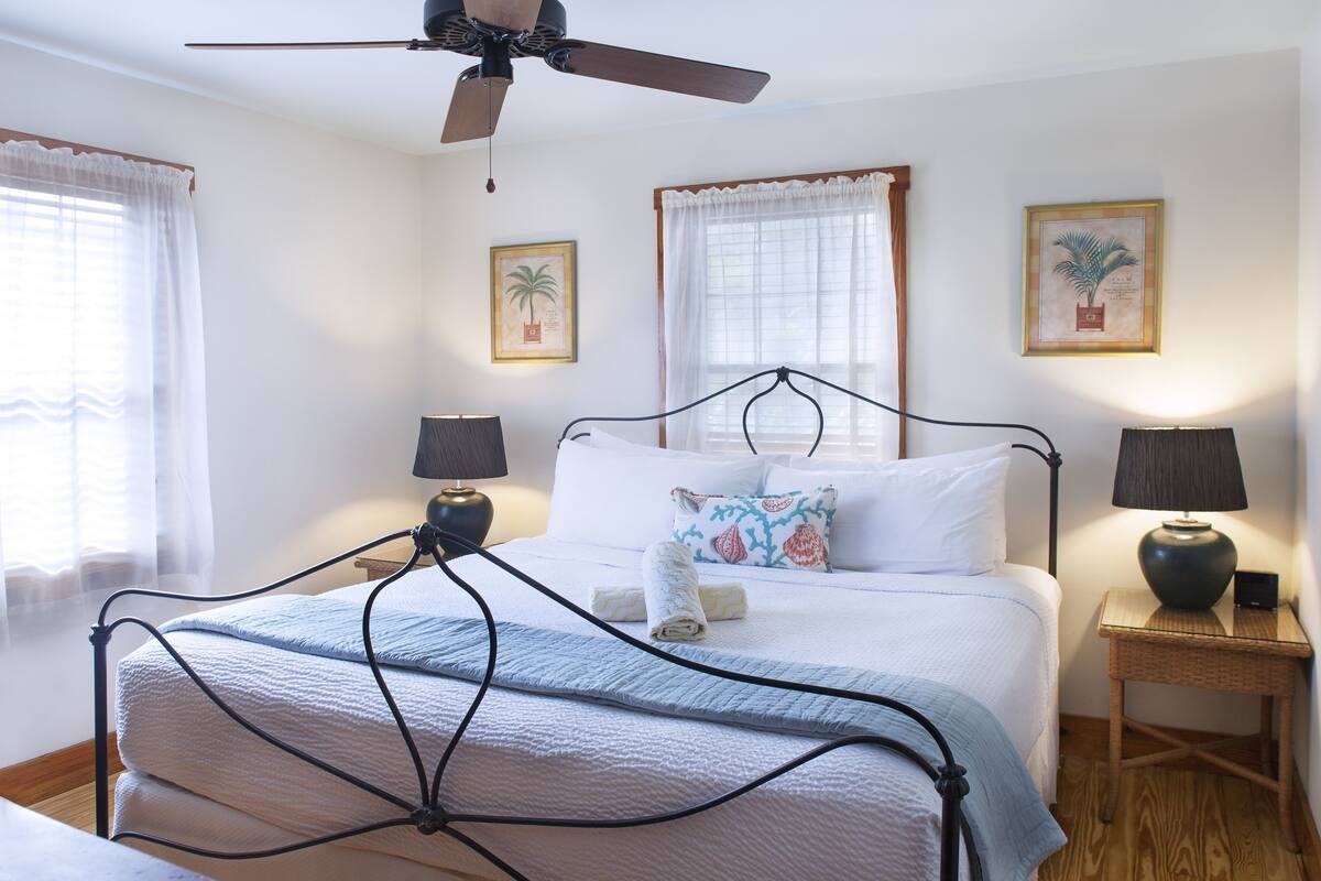 A neatly made bed with a white comforter and pillows, a ceiling fan, and two bedside tables with lamps.