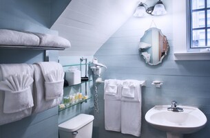 Un baño con lavamanos blanco, cabina de ducha de vidrio y toallas en un perchero.