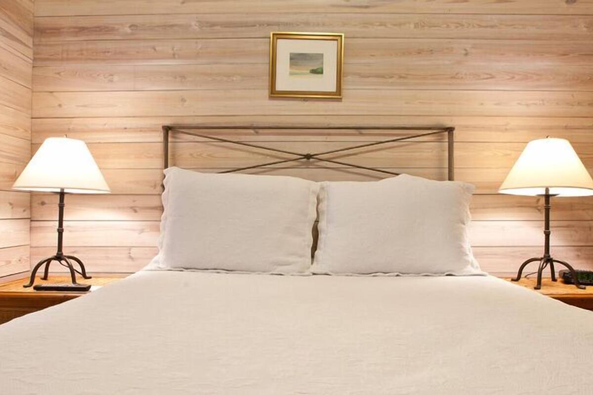 A wooden-paneled room with a bed, two bedside lamps, and a framed picture on the wall.
