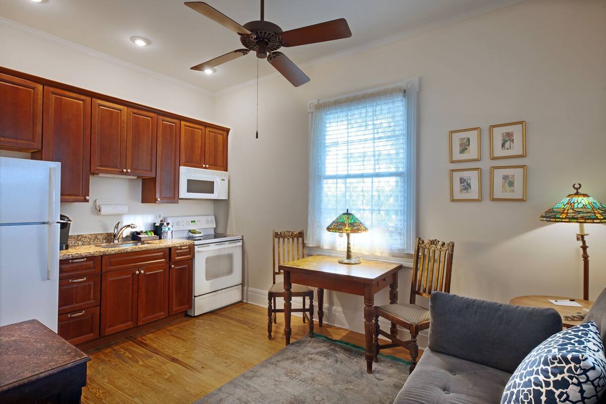 A kitchen with wooden cabinets, a refrigerator, microwave, stove, dining table with chairs, and a ceiling fan.