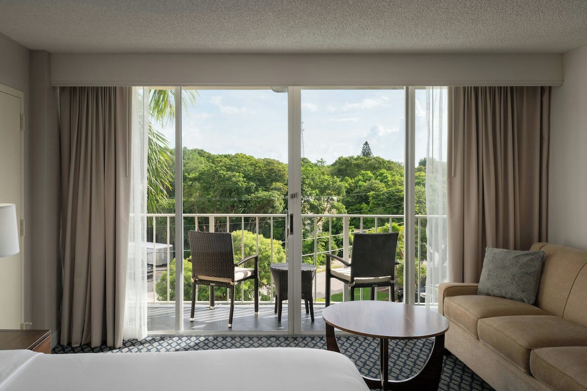 Una habitación de hotel con balcón, sofá, una mesita y dos sillas.