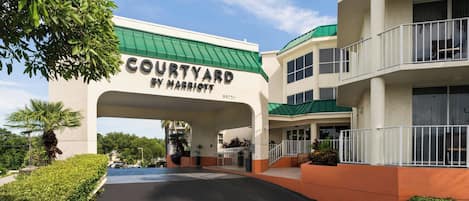 A Courtyard by Marriott hotel entrance with a green roof, a covered walkway, and a parking area.