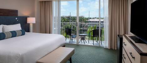 A hotel room with a large bed, a TV, a desk, and a balcony with chairs and a table.