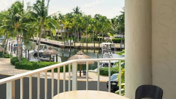 A balcony with a table and two chairs, overlooking a marina with boats and palm trees.