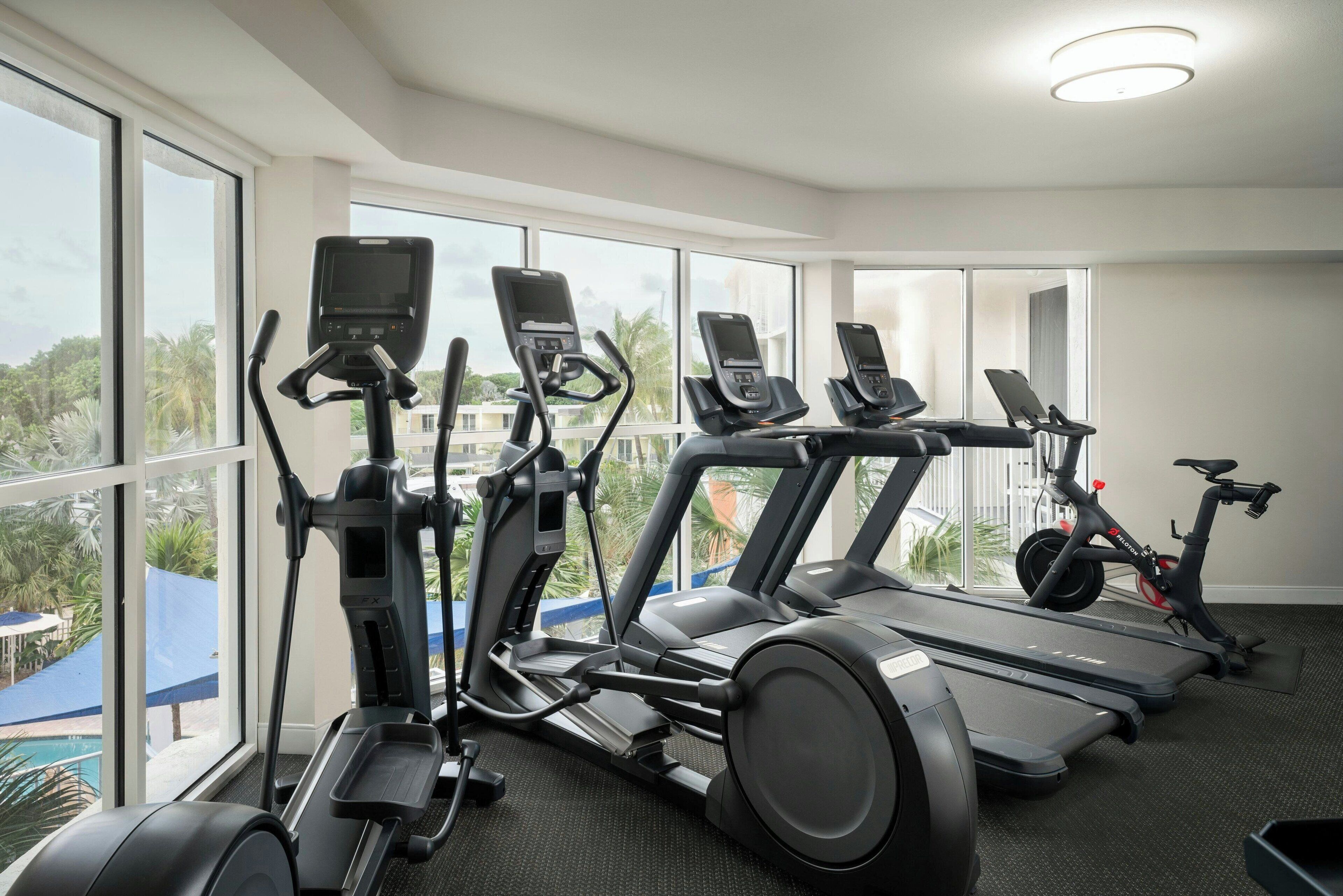 Ein Fitnessraum mit verschiedenen Cardiogeräten, großen Fenstern und Blick ins Freie.