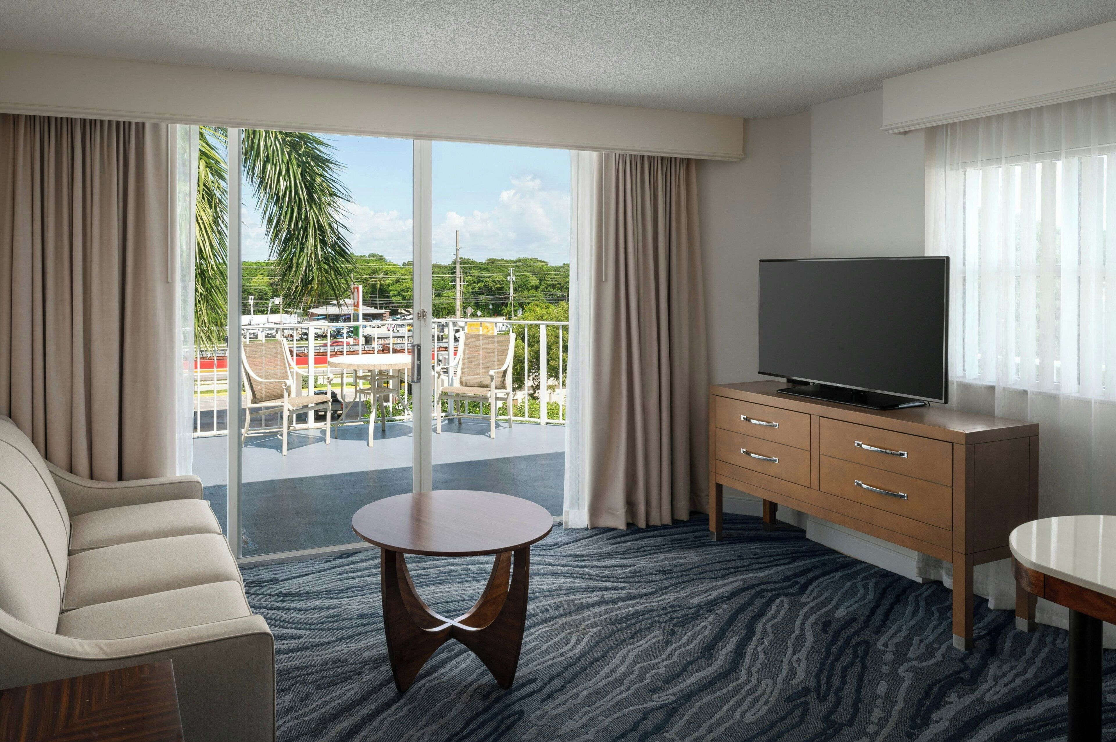 A hotel room with a balcony, a TV, a sofa, and a small table.
