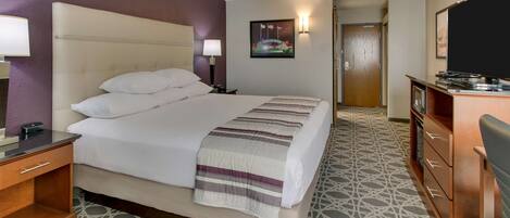 A hotel room with a large bed, a wooden dresser, a television, and a patterned floor.