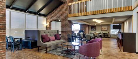 A spacious lobby with a high ceiling, a mezzanine level, and a seating area with a sofa and chairs.