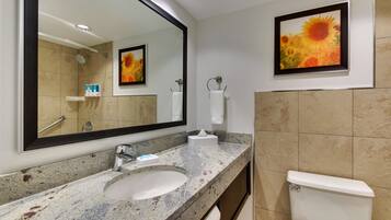 A bathroom with a granite countertop sink, a large mirror, a framed sunflower painting, a toilet, and a towel rack.