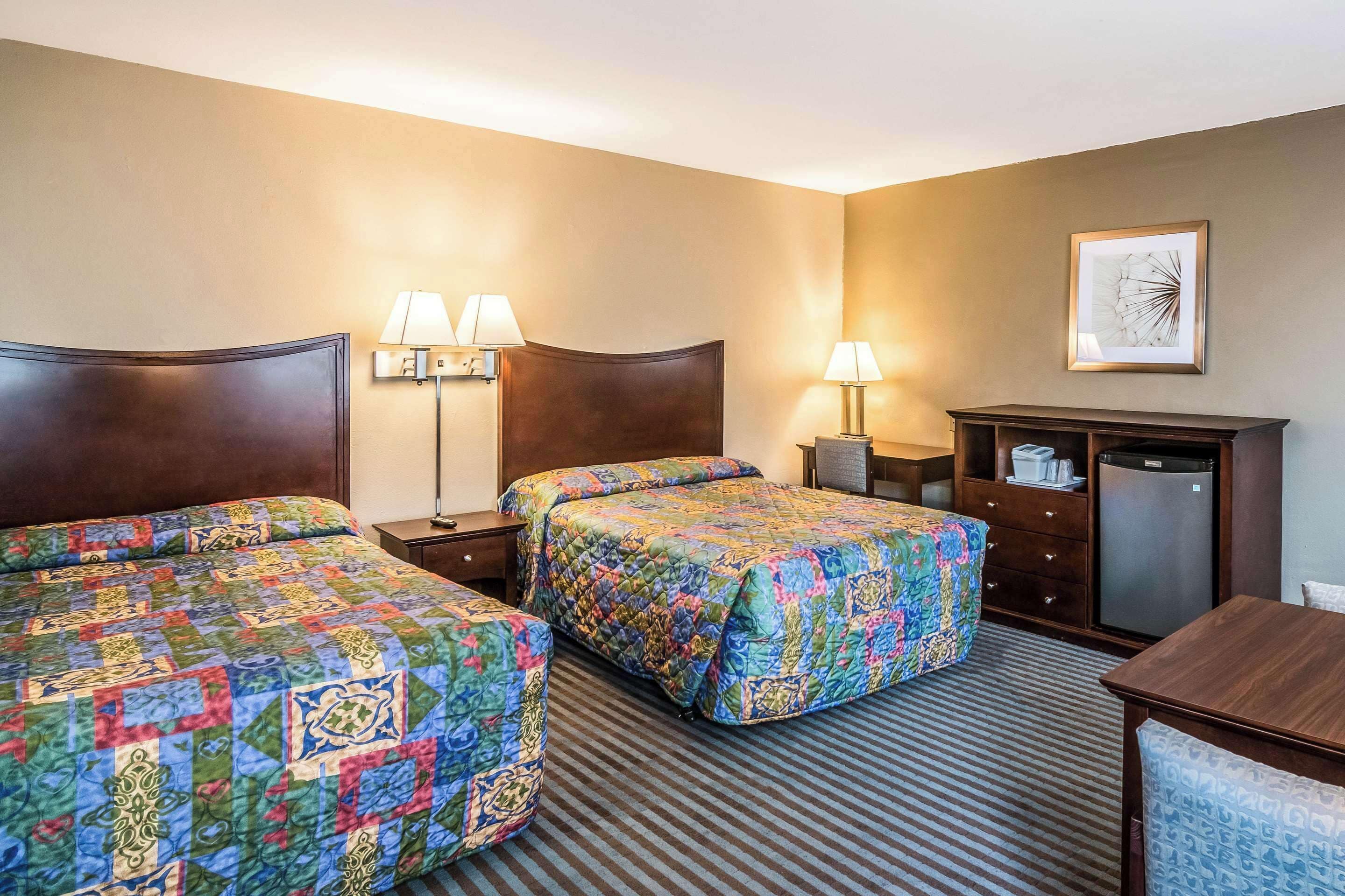 A hotel room with two beds, a desk, a dresser, and a refrigerator.