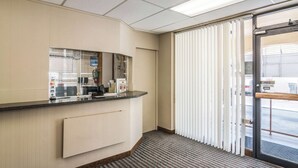 A reception area with a counter, a clock, and a window with blinds. - Rodeway Inn Regalodge (Glendale)