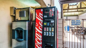 A Coca-Cola vending machine and a refrigerator near a pool area gate. - Rodeway Inn Regalodge (Glendale)