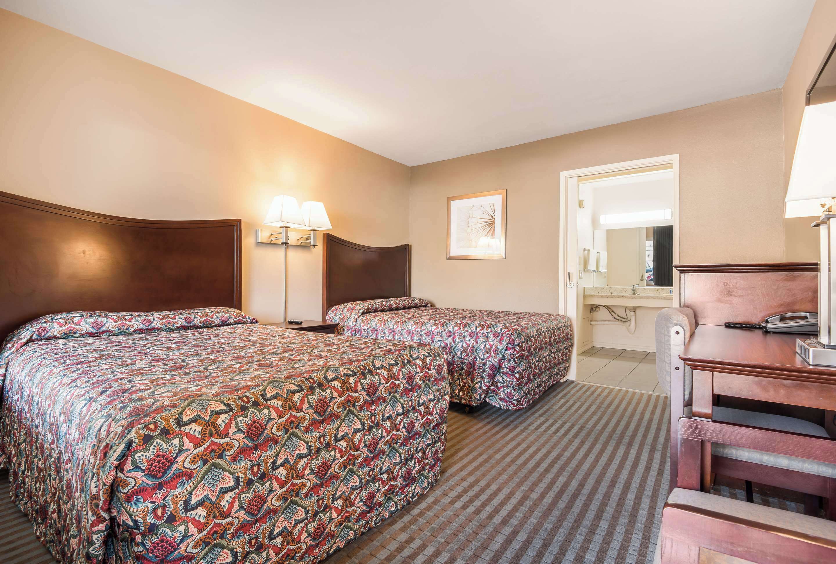 A hotel room with two beds, a desk, a chair, a lamp, and a mirror.