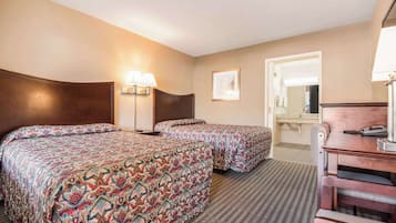 A hotel room with two beds, a desk, a chair, a lamp, and a mirror.