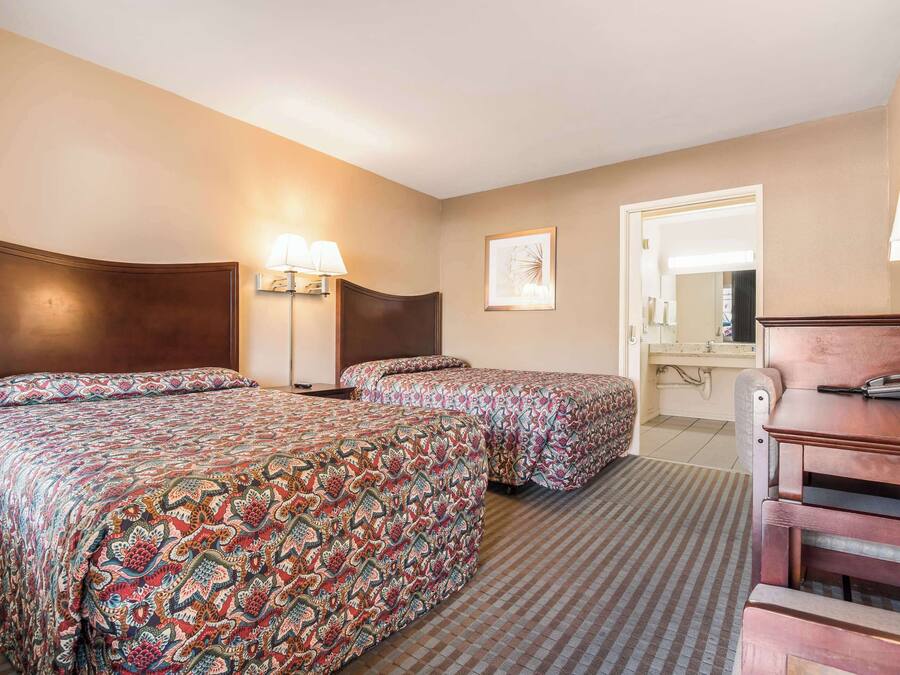 A hotel room with two beds, a desk, a chair, a lamp, and a mirror.