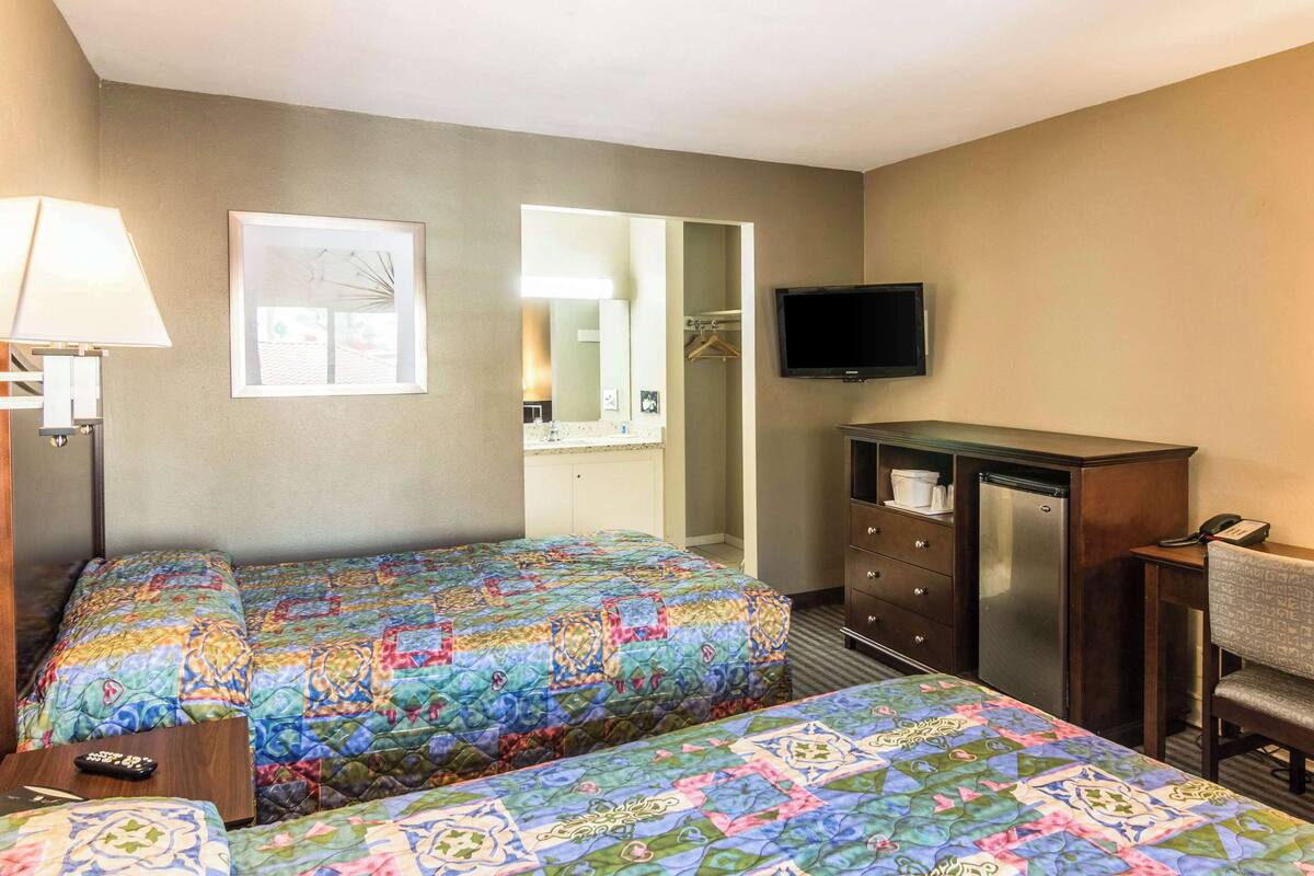 A hotel room with two beds, a TV, a dresser, and a desk with a chair.