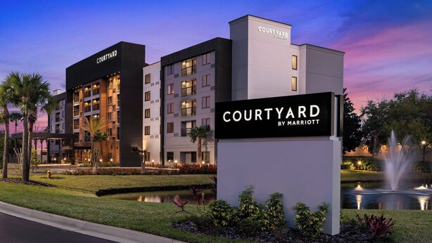 A Courtyard by Marriott hotel with a modern design, a signboard, and a landscaped garden with a fountain. - Courtyard by Marriott Jacksonville Butler Boulevard (Jacksonville)