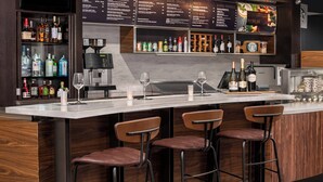 A bar area with a menu board, bar stools, and a variety of bottles.