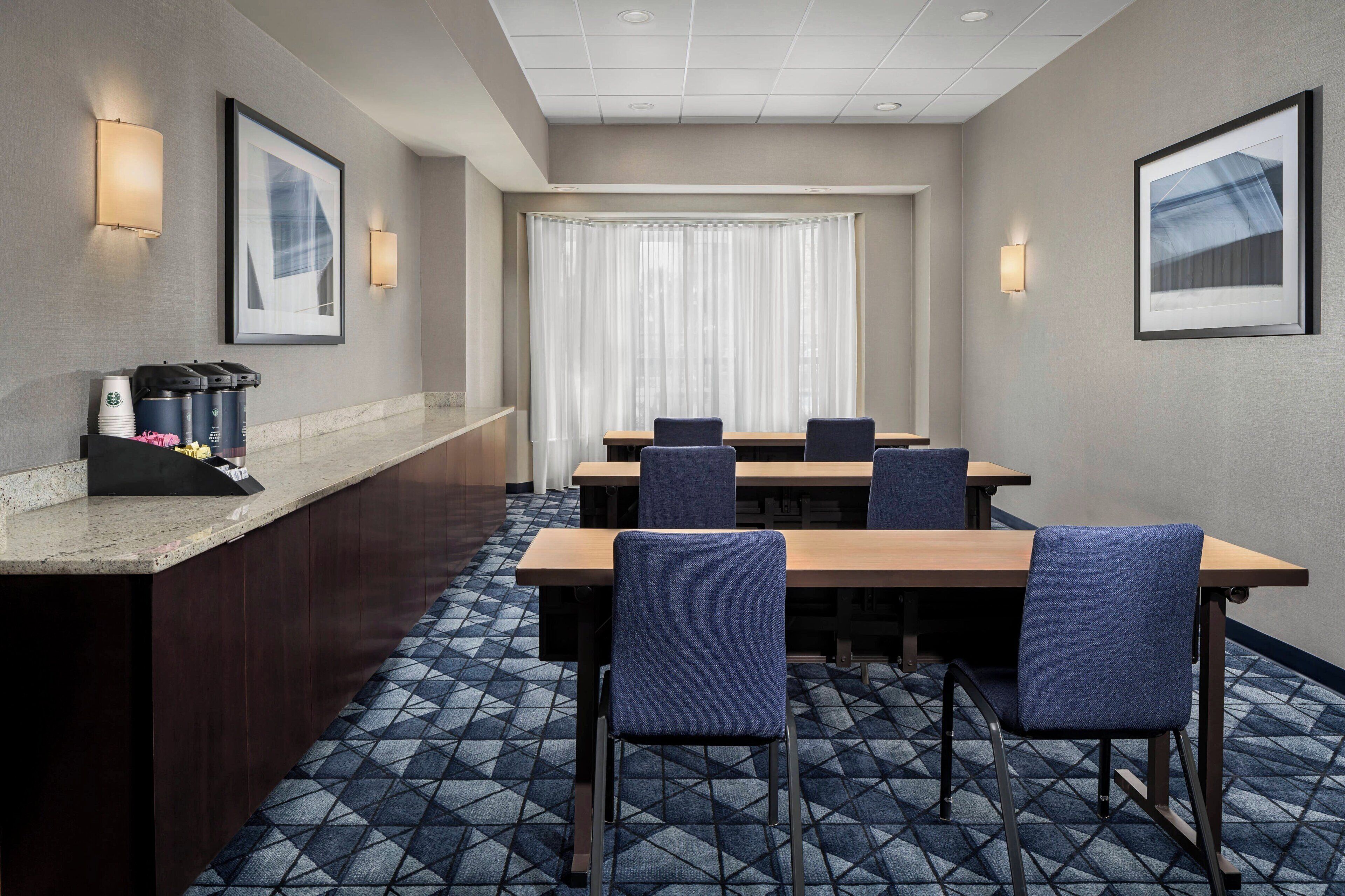 A conference room with a long table, four chairs, a coffee station, and framed artwork on the walls.