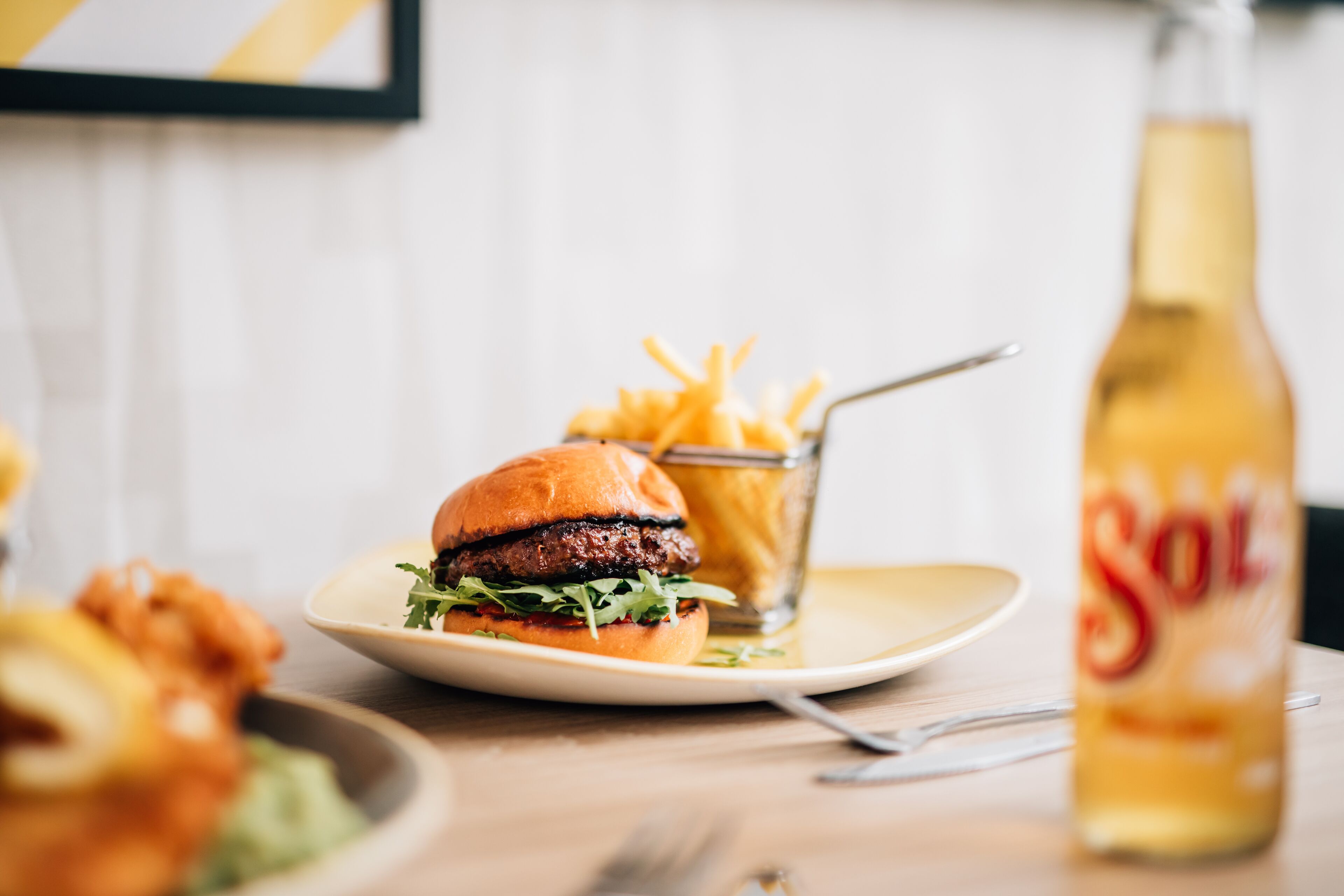 A burger with fries and a bottle of Sol beer on a table.