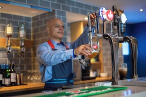 A bartender pouring a drink from a tap labeled "Guinness" in a bar setting with tiled walls and various bottles in the background. - Holiday Inn Express Belfast City by IHG (Belfast)