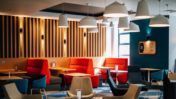 A modern cafe with wooden slat walls, red and blue seating, and pendant lighting. - Holiday Inn Express Belfast City by IHG (Belfast)