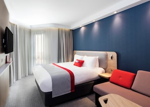 A modern hotel room with a bed, a TV, a bedside table, and a seating area. - Holiday Inn Express Belfast City by IHG (Belfast)