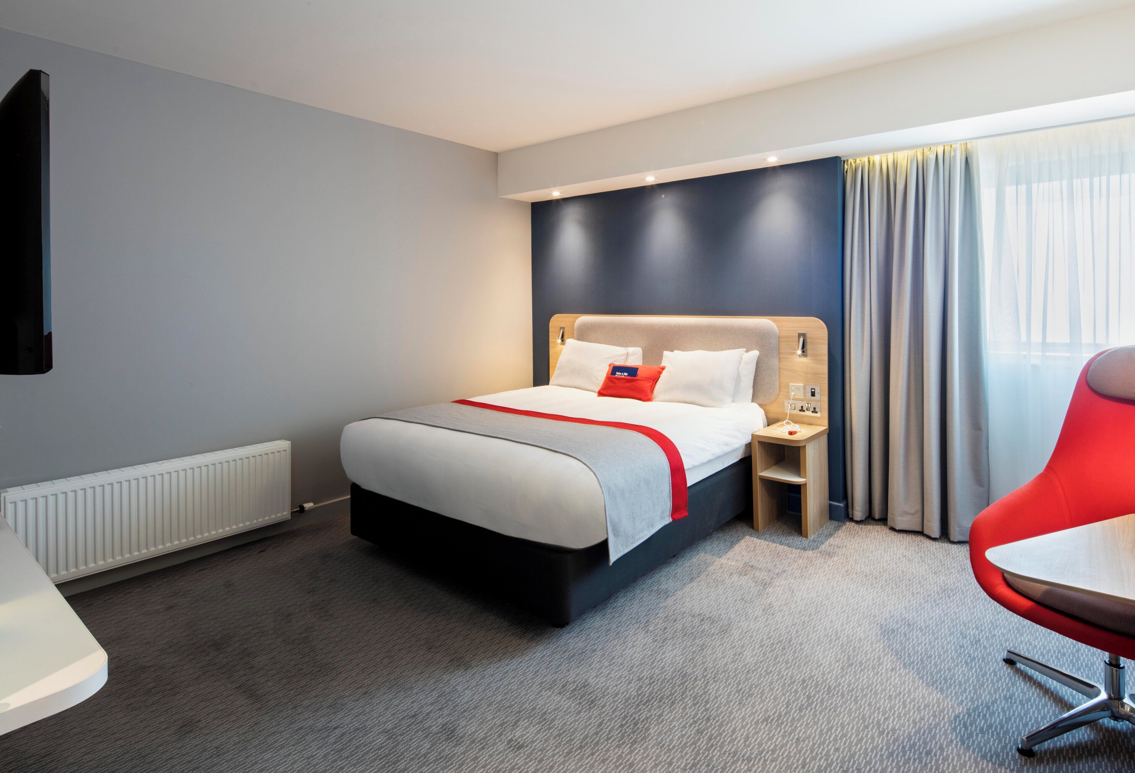 A hotel room with a bed, bedside table, chair, and a view of the outdoors.