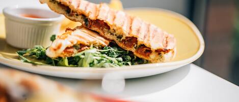 A sandwich on a plate with a side salad and a small bowl of sauce.