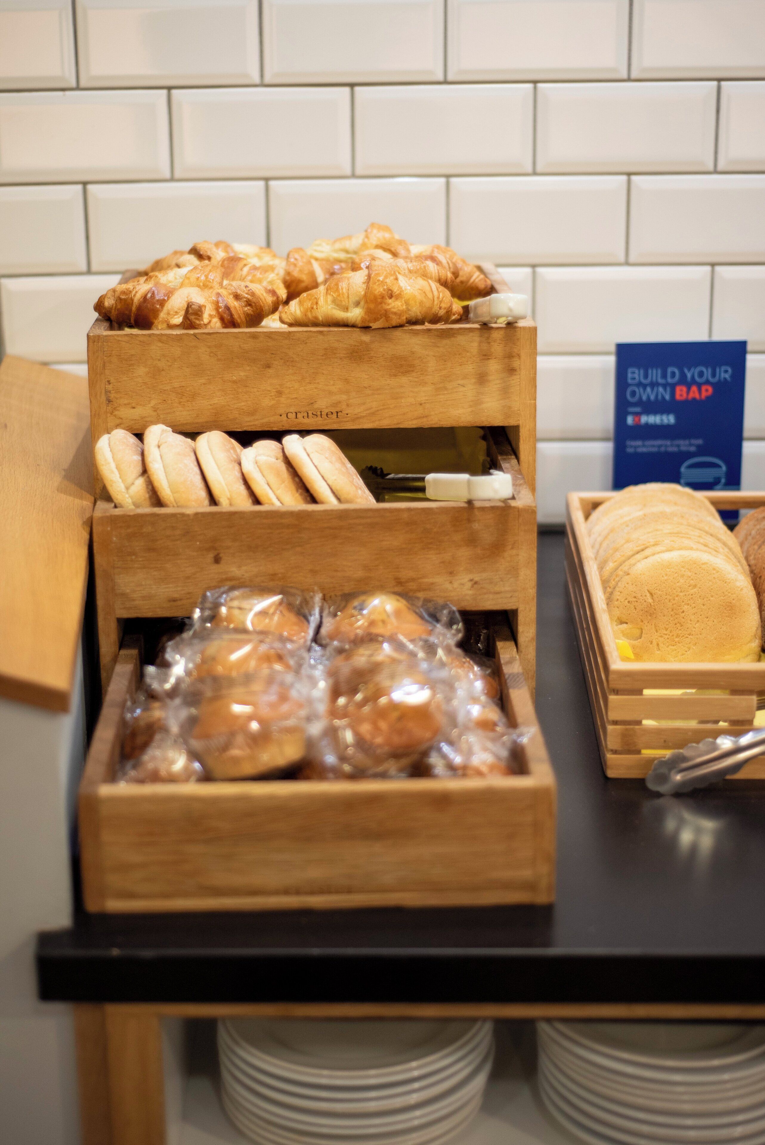 Un expositor de madera con diversas opciones de panadería, incluyendo croissants y pan.