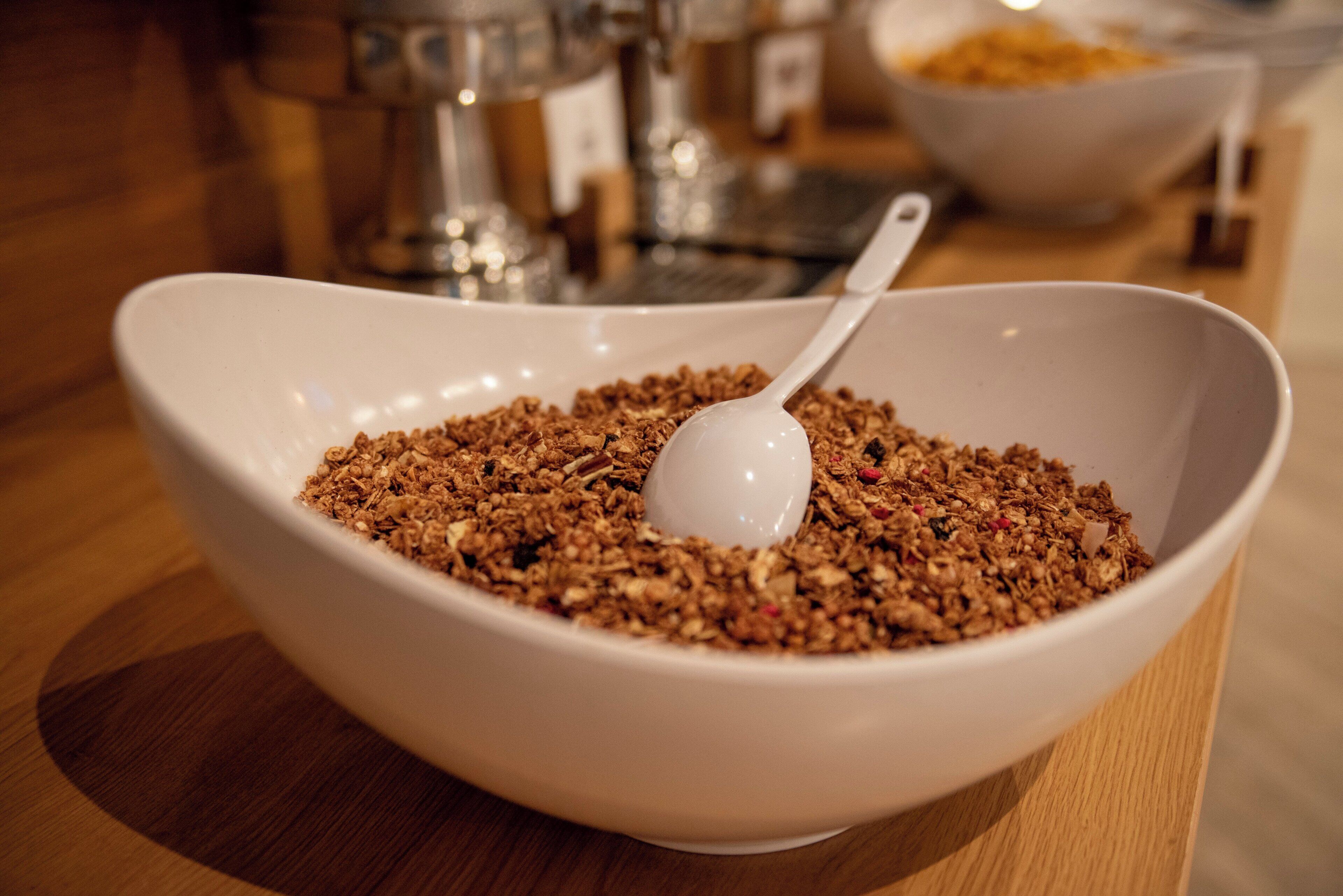 A white bowl filled with granola and a spoon, placed on a wooden table.