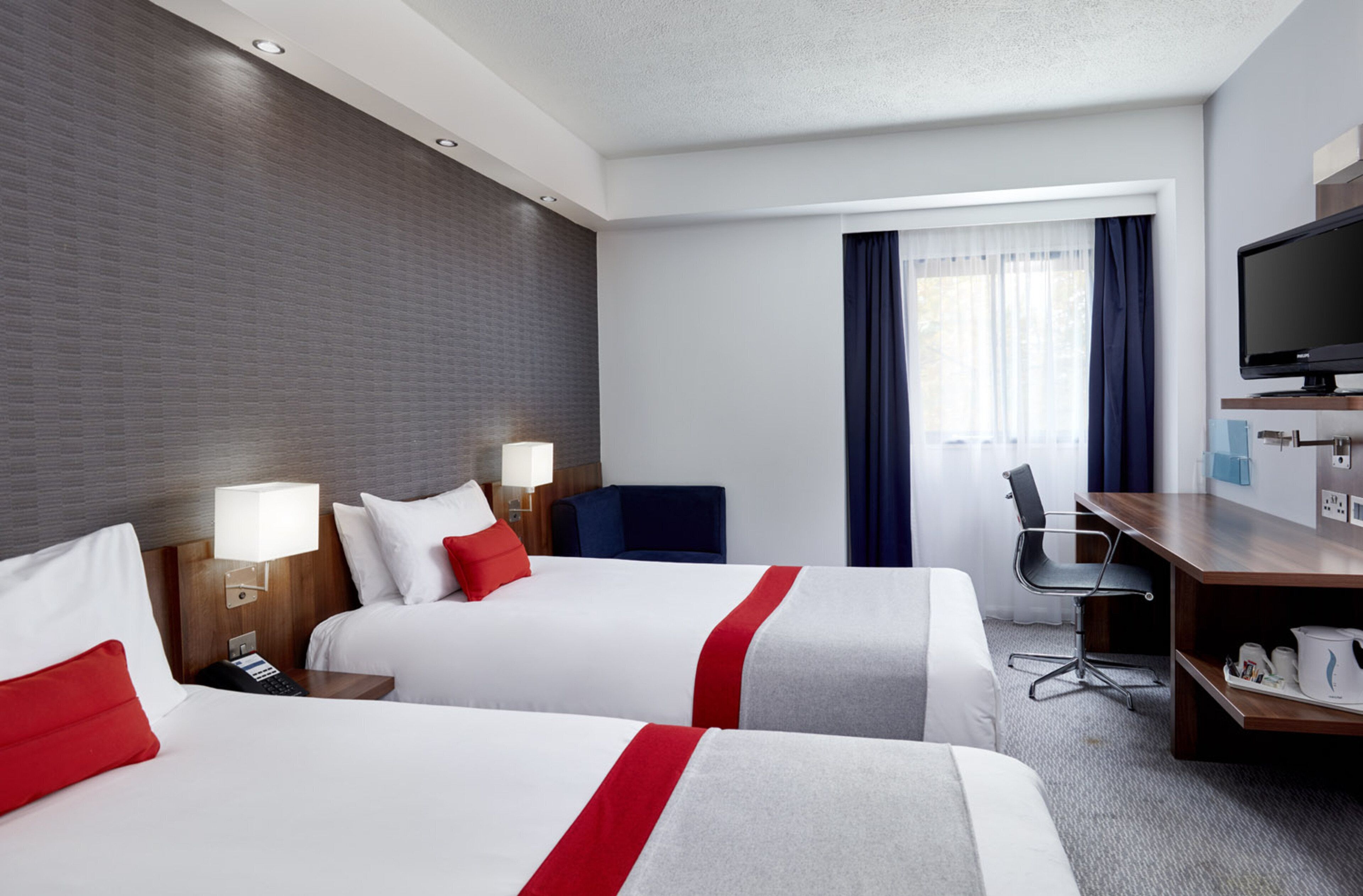 Habitación de hotel con dos camas, un escritorio, una silla, un televisor y una ventana con cortinas.