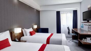 Habitación de hotel con dos camas, un escritorio, una silla, un televisor y una ventana con cortinas.