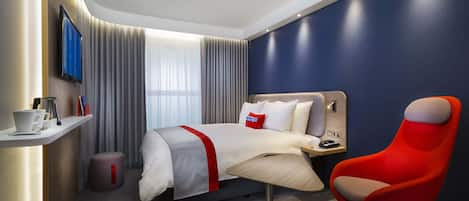 Una habitación de hotel moderna con una cama, una silla roja, un televisor y un escritorio con una lámpara.