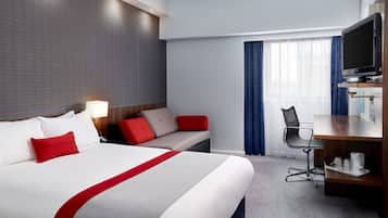 Una habitación de hotel con una cama grande, un escritorio con silla, televisor y ventana con cortinas.