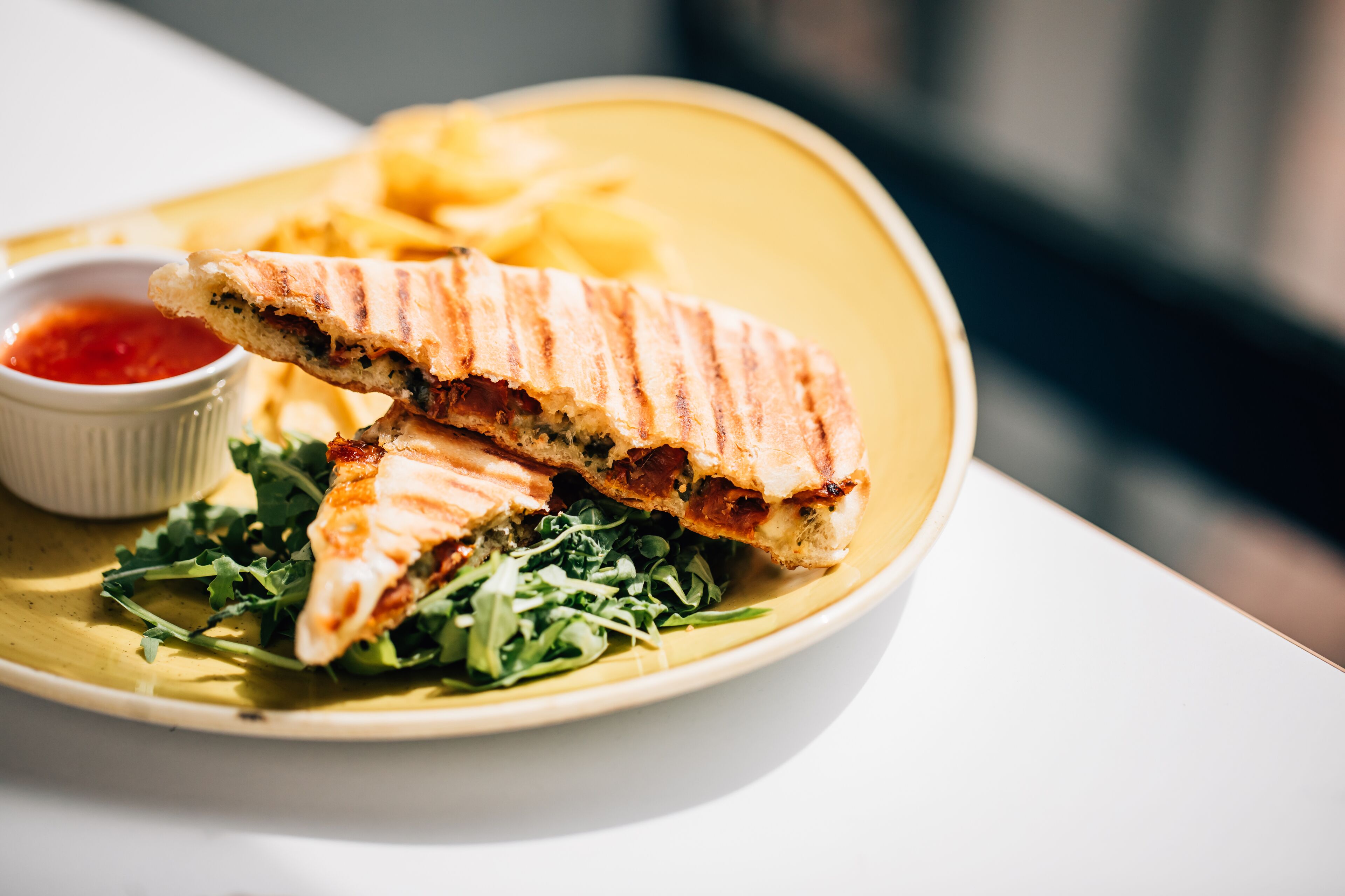Ein Sandwich mit Pommes und einer kleinen Ketchup-Schale auf einem gelben Teller.