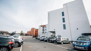 A parking lot with multiple cars parked in front of a modern building with a white facade and a brick structure in the background.
